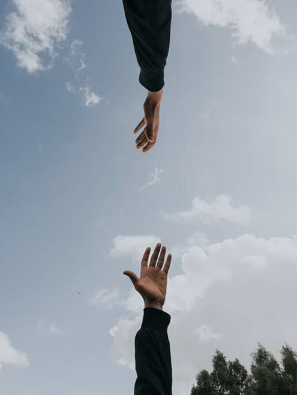 This is a photo of two hands reaching for each other. The background is the sky.