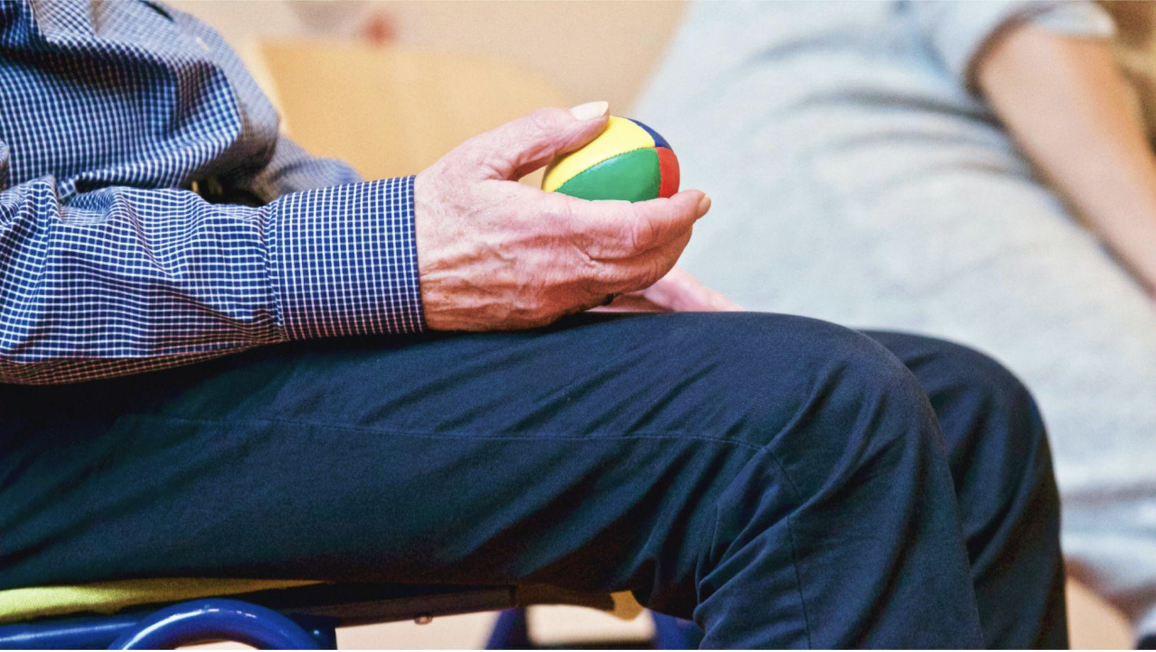This is a photo of an elderly man siting down and holding a small colourful ball.