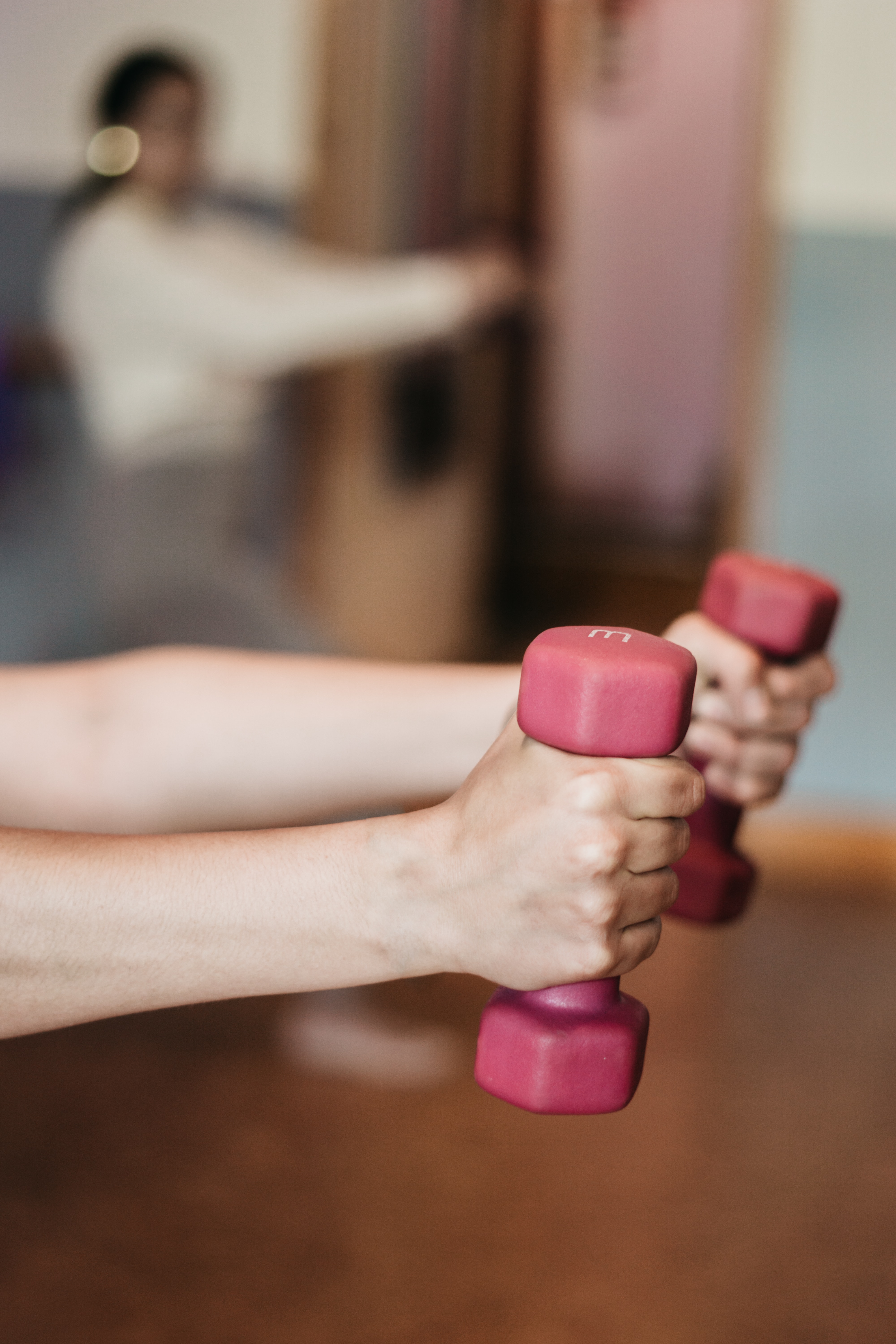 Decorative photo of two hands holding pink weight bars across the body.